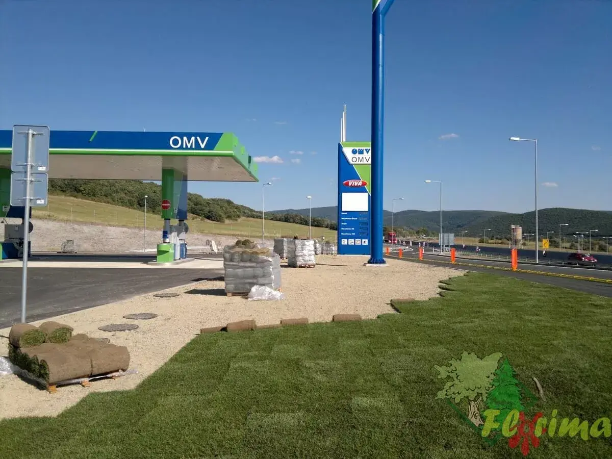 Čerpacia stanica OMV vo výstavbe s dokončovanými terénnymi úpravami, čerstvo položeným trávnikom a panoramatickým výhľadom na okolité kopce